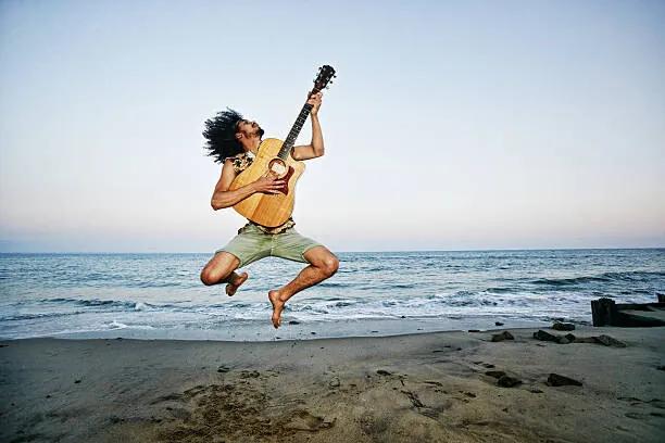 Kunstfotografie Mixed Race man playing guitar and jumping at beach, Peathegee Inc, (40 x 26.7 cm)