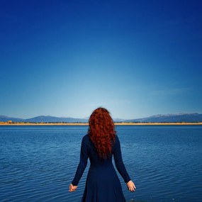 Kunstfotografie Redhead in blue dress faces rippled lake, Anna Gorin, (40 x 40 cm)