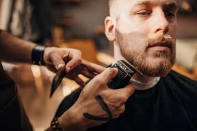 Foto Male barber cutting beard of client in barber shop, South_agency